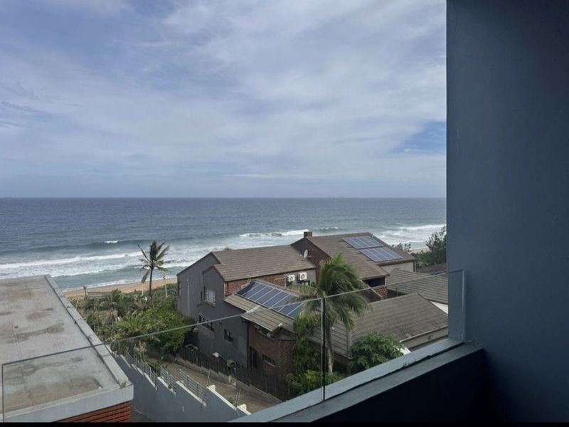 A scenic elevated view of the ocean and coastline, captured from a balcony with a modern glass balustrade.