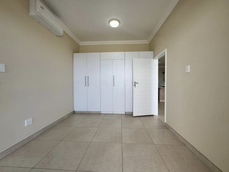 A clean, empty bedroom featuring neutral tiled floors, built-in white cupboards, and a wall-mounted air conditioning unit.