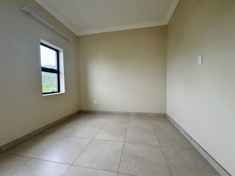 A clean, empty bedroom featuring neutral tiled flooring, coved ceilings, and a window providing natural light.