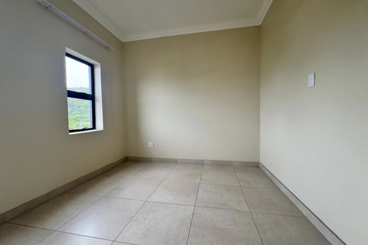 A clean, empty bedroom featuring neutral tiled flooring, coved ceilings, and a window providing natural light.