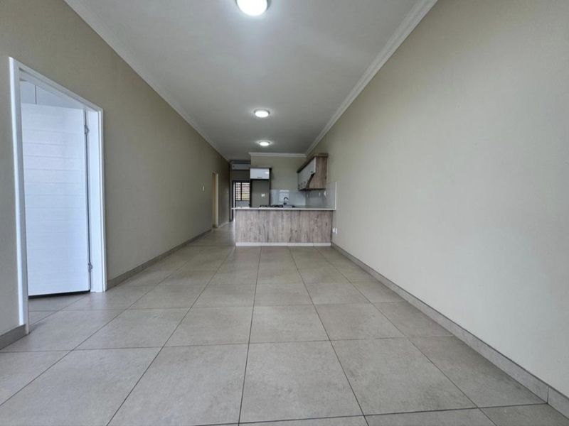 An open-plan living and kitchen area featuring neutral tiled flooring, modern cabinetry, and recessed lighting, offering a clean and versatile space.