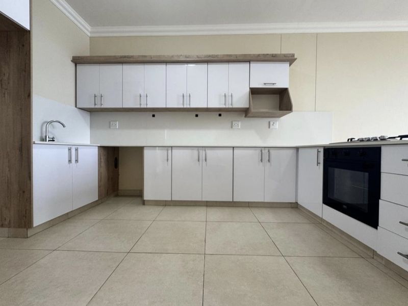 Modern kitchen featuring white cabinetry, wood-look accents, tiled flooring, and integrated oven and hob, offering a clean and functional workspace.