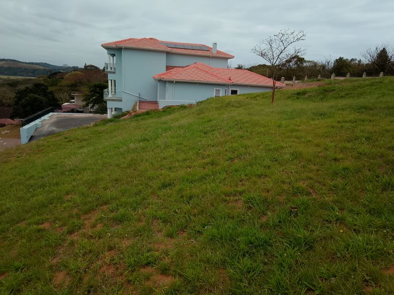 A view of the rear elevation of the residential property, featuring a multi-level structure with a tiled roof and solar panels, set on a sloped lot.