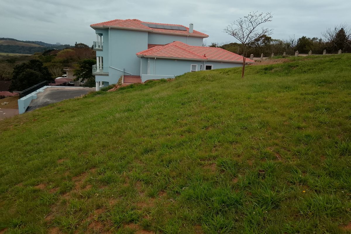 A view of the rear elevation of the residential property, featuring a multi-level structure with a tiled roof and solar panels, set on a sloped lot.