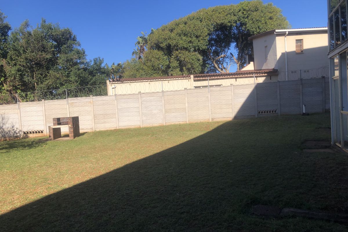 A private rear garden featuring a lawn area, a built-in brick braai, and secure perimeter walling with razor wire.