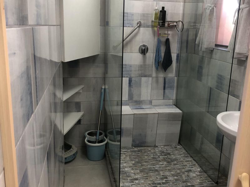 A functional bathroom featuring a glass-enclosed shower with a built-in seat, tiled walls, and a pedestal basin.