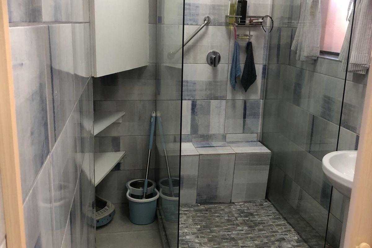A functional bathroom featuring a glass-enclosed shower with a built-in seat, tiled walls, and a pedestal basin.