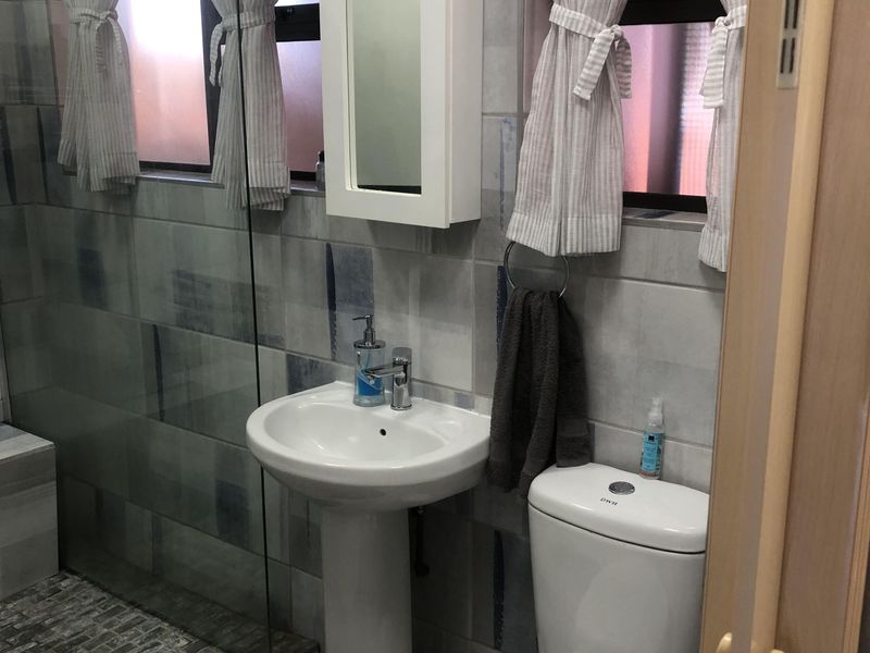 A functional bathroom featuring a pedestal basin, toilet, and a glass-enclosed shower with decorative wall tiling.