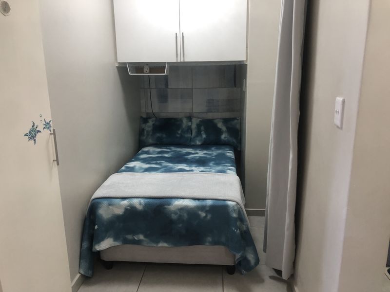 A compact bedroom featuring built-in overhead cabinetry, tiled flooring, and a built-in wardrobe, providing efficient storage solutions in a small footprint.