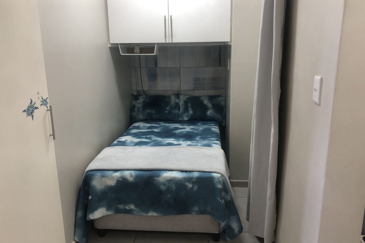 A compact bedroom featuring built-in overhead cabinetry, tiled flooring, and a built-in wardrobe, providing efficient storage solutions in a small footprint.