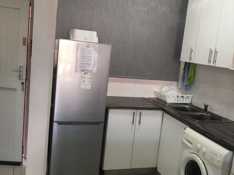 Compact kitchen featuring white cabinetry, dark laminate countertops, double basin sink, and tiled flooring with integrated laundry plumbing.