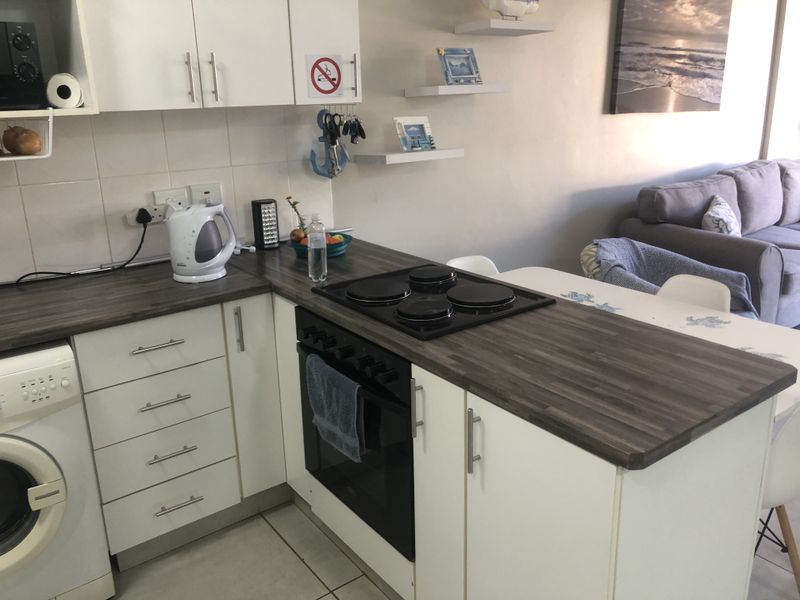 Compact open-plan kitchen featuring white cabinetry, dark laminate countertops, built-in oven and hob, and tiled flooring, seamlessly flowing into the living area.