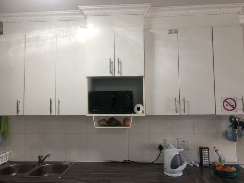 A functional kitchen area featuring white built-in cabinetry, a double bowl stainless steel sink, laminate countertops, and classic crown molding detail.