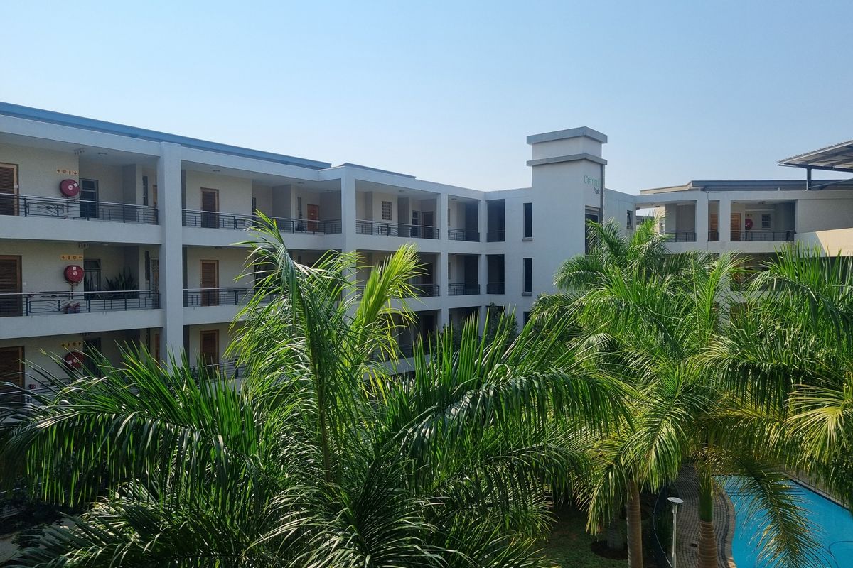An elevated view of the apartment complex featuring multiple levels of balconies, a swimming pool, and surrounding palm trees.