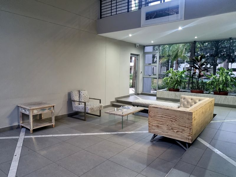 A spacious, modern living area featuring double-volume ceilings, large glass windows, and tiled flooring with a contemporary open-plan layout.