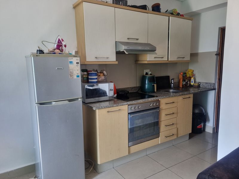 Compact kitchen featuring light wood cabinetry, granite countertops, integrated oven and hob, and tiled flooring.
