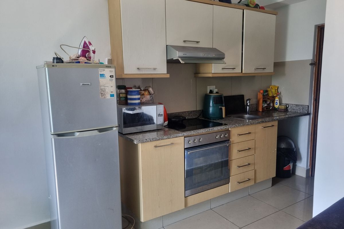 Compact kitchen featuring light wood cabinetry, granite countertops, integrated oven and hob, and tiled flooring.
