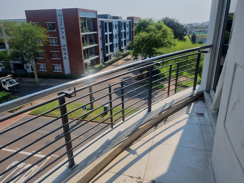 A clean, tiled balcony featuring a modern metal balustrade, offering an elevated view of the surrounding apartment complex and street.