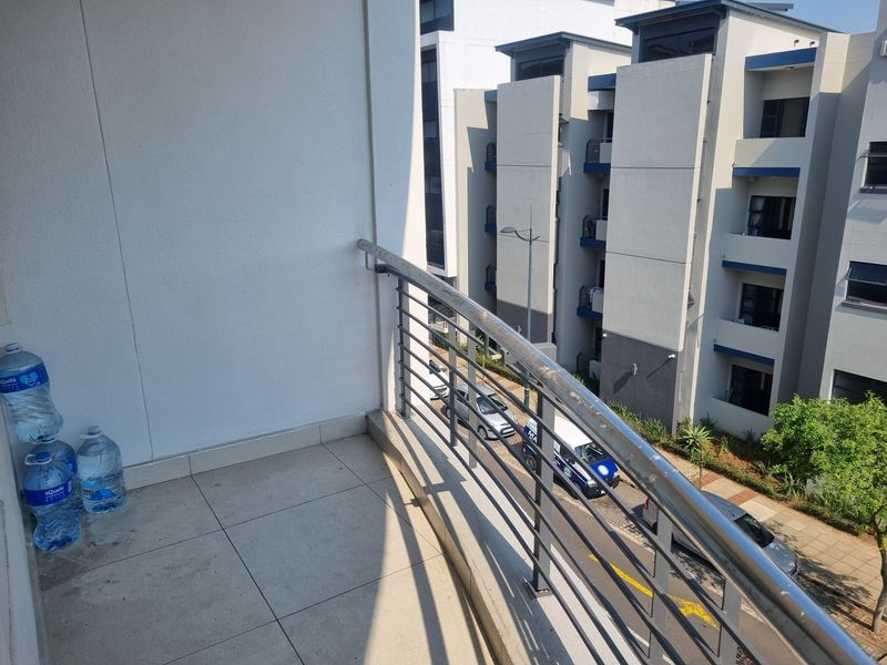 A private apartment balcony featuring tiled flooring and a modern stainless steel balustrade, overlooking the complex grounds and street.
