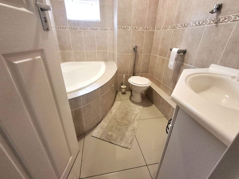 A functional bathroom featuring a corner bathtub, toilet, and vanity basin with neutral wall and floor tiling.