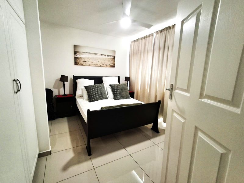 A well-maintained bedroom featuring neutral tiled flooring, built-in cupboards, and a ceiling fan, offering a clean and functional living space.