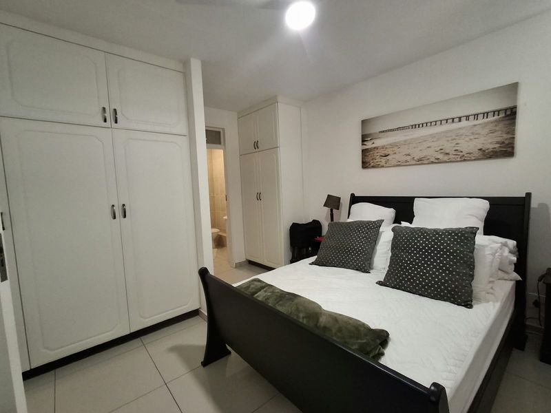 A bedroom featuring built-in cupboards and tiled flooring, with an adjoining bathroom visible in the background.