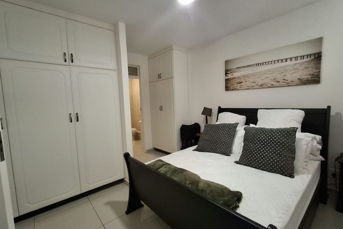 A bedroom featuring built-in cupboards and tiled flooring, with an adjoining bathroom visible in the background.