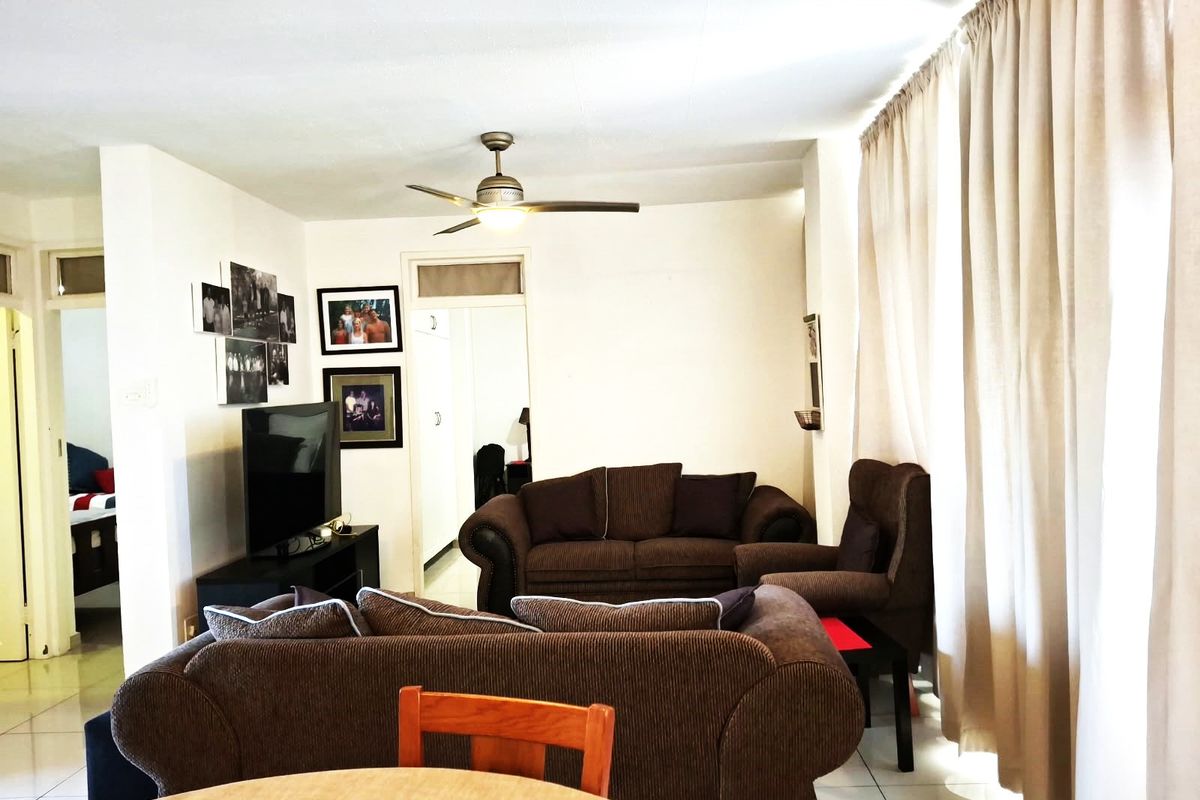 A living room area featuring tiled flooring and a ceiling fan, with natural light entering through large window curtains.
