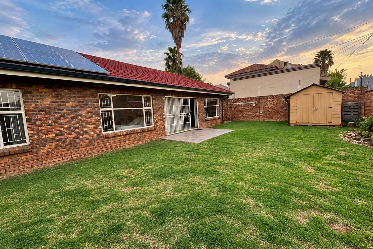 Rear view of the property featuring a brick exterior, solar panels on the roof, a well-maintained lawn, and a secure garden shed.
