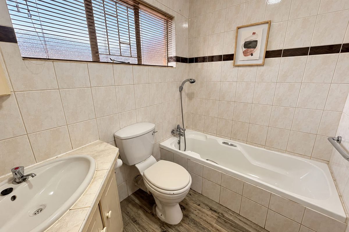 A functional bathroom featuring a built-in vanity, toilet, and bathtub with a handheld shower mixer, finished with tiled walls and wood-look flooring.