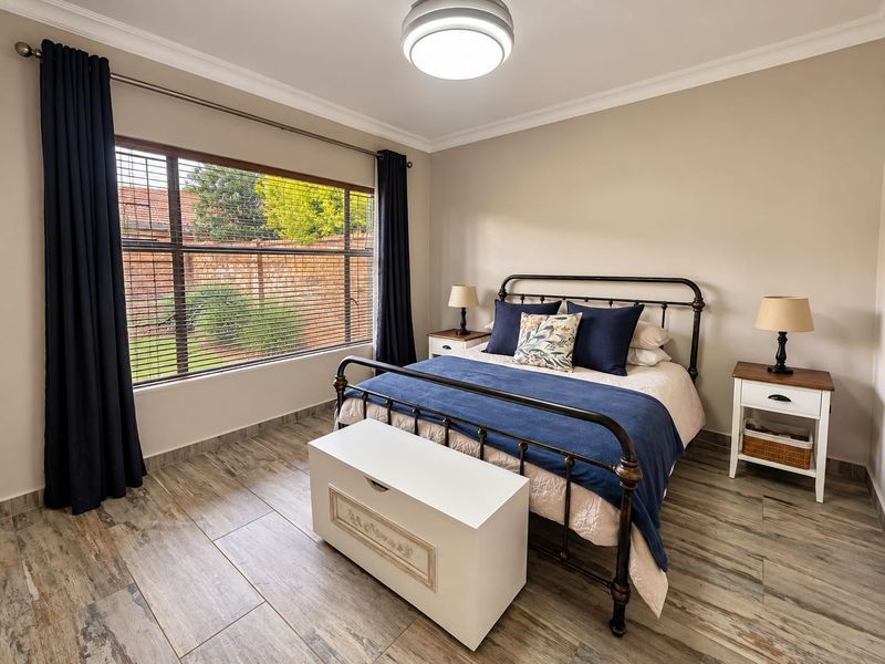 A well-maintained bedroom featuring wood-look tile flooring, neutral wall tones, and a large window providing natural light.