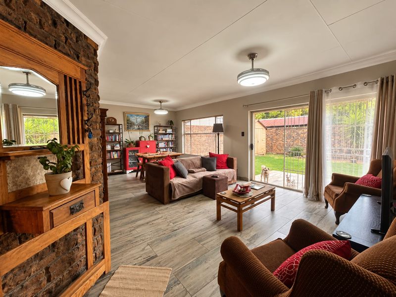 Spacious open-plan living area featuring an exposed brick wall, wood-look tiled flooring, and sliding glass doors providing direct access to the rear garden.