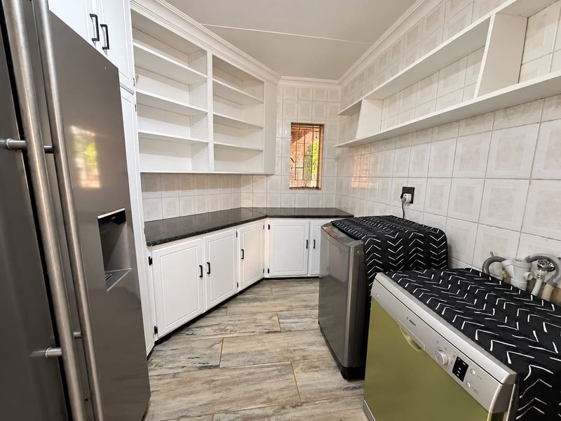 A well-maintained scullery featuring ample built-in cabinetry, granite countertops, tiled splashbacks, and dedicated plumbing connections for laundry appliances.