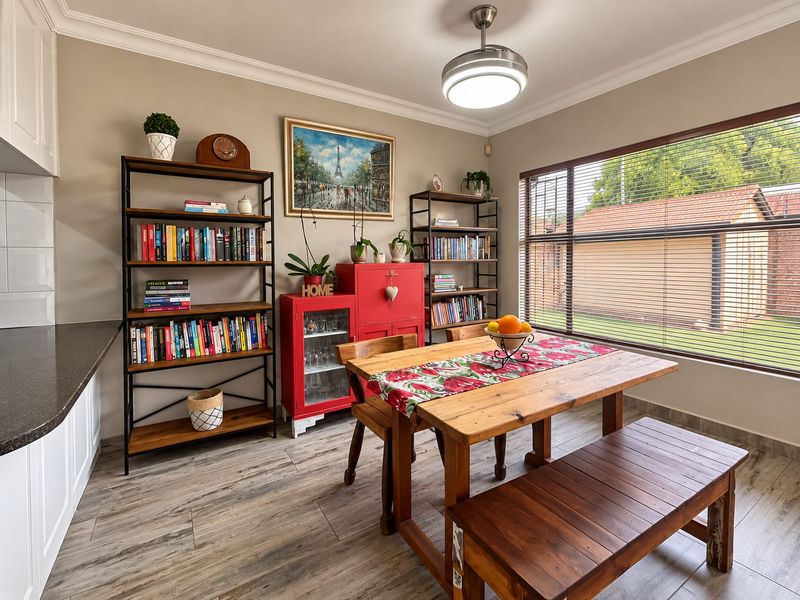 A well-maintained dining area featuring tiled flooring, crown molding, a ceiling fan, and large windows with venetian blinds, adjacent to the kitchen workspace.