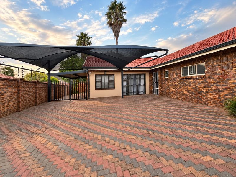 A well-maintained front exterior featuring extensive brick paving, a large shade sail structure, and secure face brick boundary walls.
