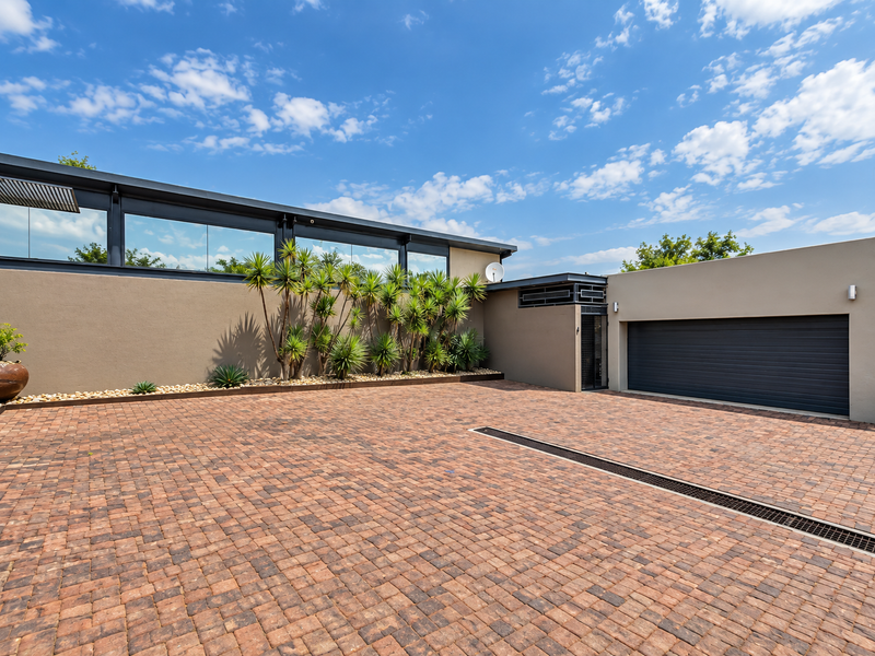 Modern front exterior featuring a spacious paved driveway, a large sectional garage door, and architectural clerestory windows with clean, contemporary lines.