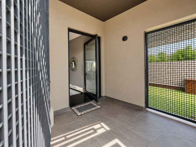 A modern, well-maintained entrance foyer featuring tiled flooring, a secure metal gate, and a glass door leading into the home.