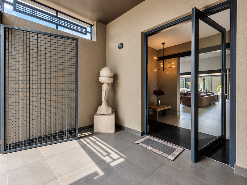 Modern covered entrance area featuring large format floor tiles, a secure metal gate, and a sleek pivot door leading into the home.