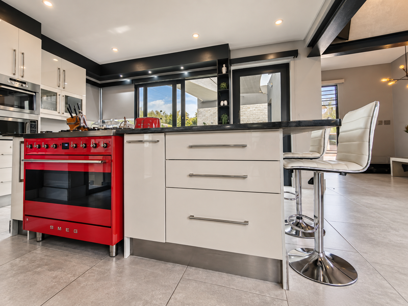 Modern kitchen featuring a striking red Smeg range cooker, central island with stone countertop, and sleek cabinetry, opening onto an outdoor patio area.