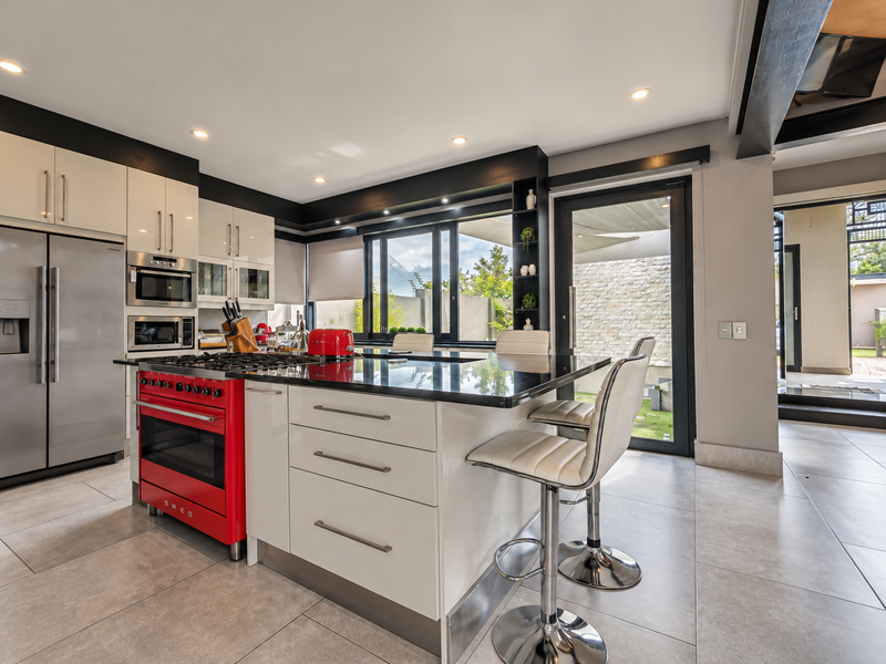 Modern kitchen featuring a central island with stone countertops, a striking red Smeg oven, integrated appliances, and direct access to the outdoor patio area.