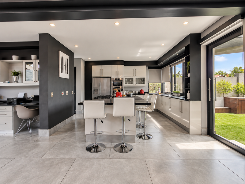 Modern open-plan kitchen featuring a central island, sleek cabinetry, built-in appliances, and seamless access to the outdoor garden area through sliding glass doors.