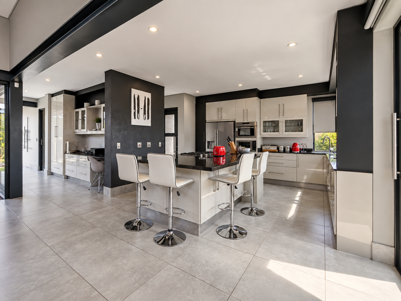 Modern open-plan kitchen featuring high-gloss cabinetry, a central island with breakfast bar seating, stone countertops, and integrated appliances.