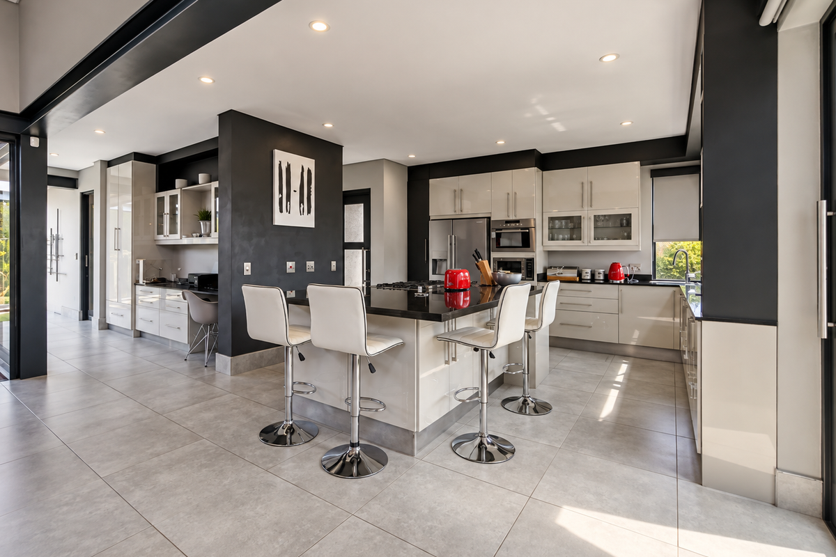 Modern open-plan kitchen featuring high-gloss cabinetry, a central island with breakfast bar seating, stone countertops, and integrated appliances.