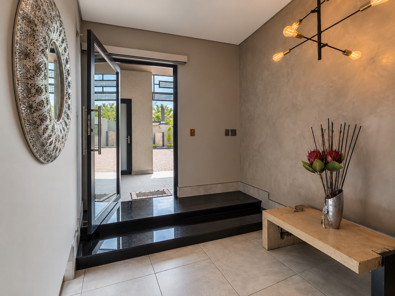 A modern entrance hall featuring a sleek pivot door, polished granite step, and contemporary lighting, creating a sophisticated and welcoming transition into the home.
