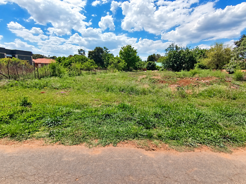 A vacant residential plot featuring overgrown grass, mature trees, and perimeter wire fencing, offering a blank canvas for future development.