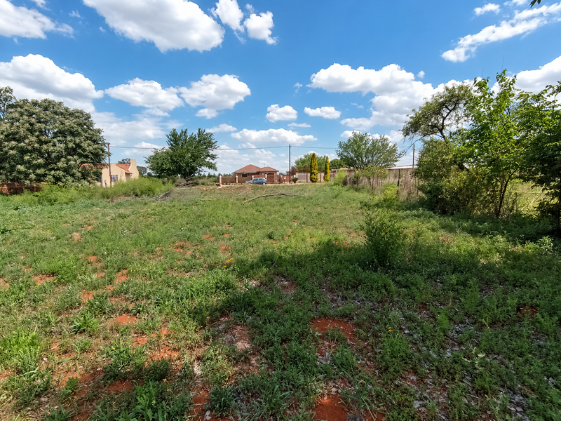 A spacious, undeveloped residential plot featuring natural vegetation, mature trees, and perimeter fencing, offering a blank canvas for future development.