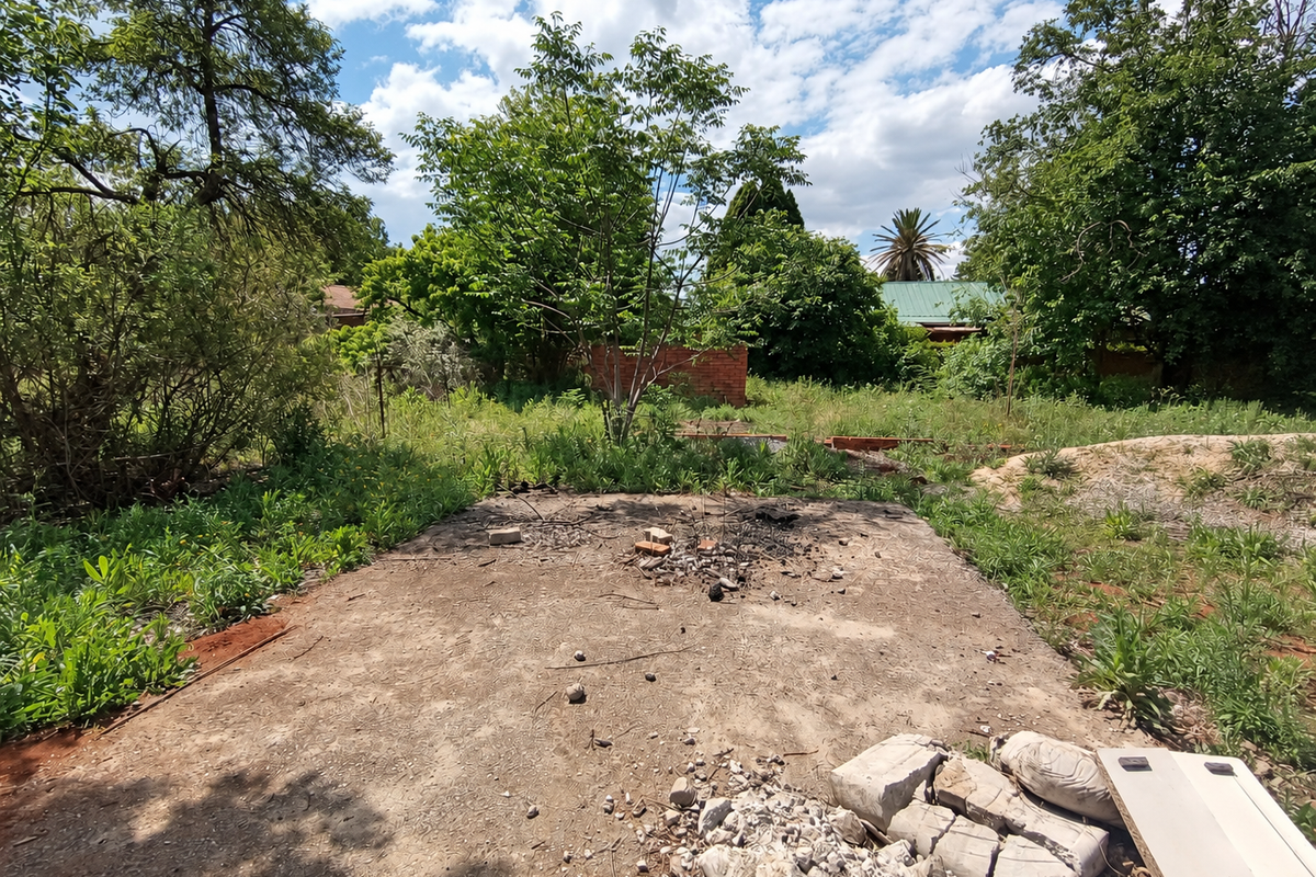 A vacant residential plot featuring a concrete slab foundation, mature trees, and overgrown vegetation, requiring site clearing and development preparation.