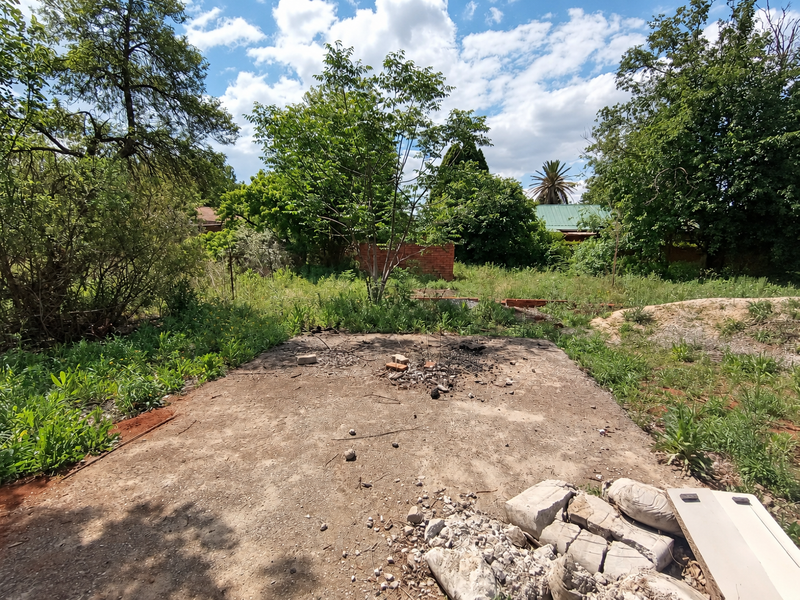 A vacant residential plot featuring a concrete slab foundation, mature trees, and overgrown vegetation, requiring site clearing and development preparation.