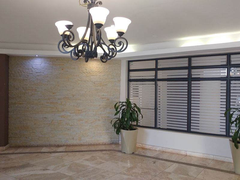 A spacious apartment entrance foyer featuring a decorative stone cladding wall, tiled flooring, and large windows with modern dark frames.