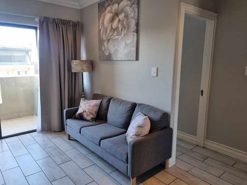 A well-maintained living area featuring modern tiled flooring, crown molding, and a sliding glass door providing access to an outdoor balcony.